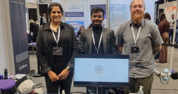 Three people stand behind a display table at an exhibition event