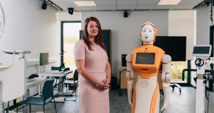 This image features a woman standing next to a humanoid robot in a modern laboratory