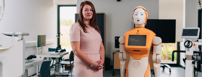 This image features a woman standing next to a humanoid robot in a modern laboratory