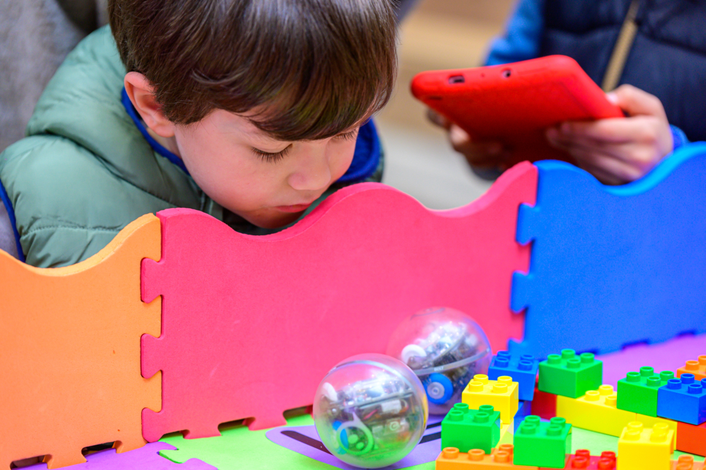 a young boy with dark brown hair looks over an activity with spherical robot and colourful lego bricks