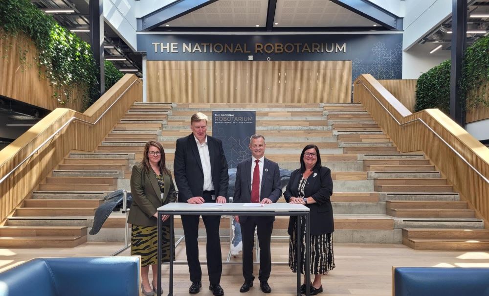 A group of four individuals standing behind a small table in The National Robotarium dressed formally, as part of a ceremonial event.