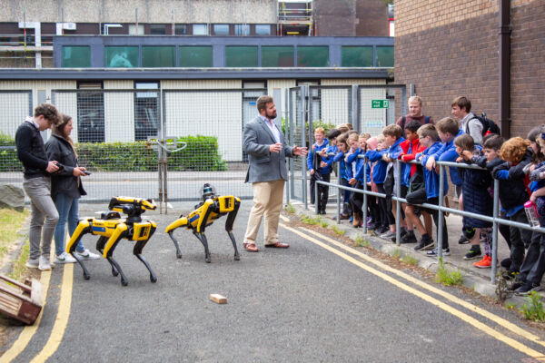 Robot dog demonstration conducted by male academic to group of primary school children
