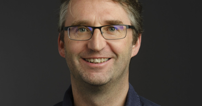 A white man with glasses and short brown hair smiling