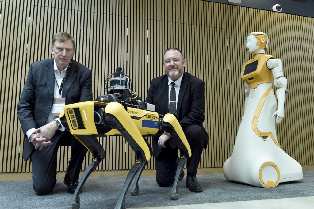 Two men in suits pose beside robot dog and humanoid robot
